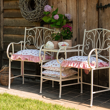 Deux chaises de jardin avec des coussins, une table avec des plantes et des coussins.