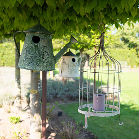 A pair of hanging watering cans and a birdcage with a candle inside