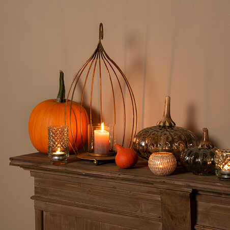 A cage with a candle in it and a pumpkin beside it.