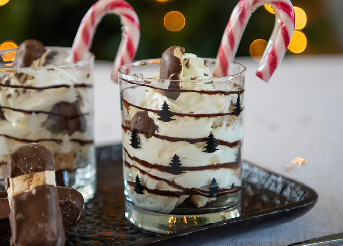 Transparent glass with black Christmas trees filled with a delicious dessert and a candy cane