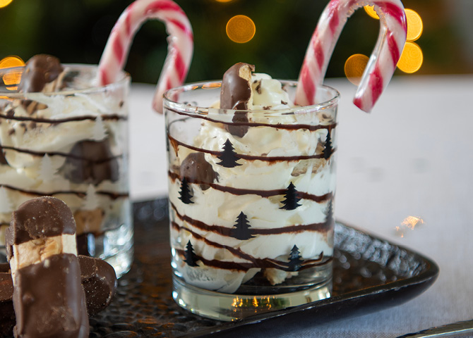 Transparentes Glas mit schwarzen Weihnachtsbäumen, gefüllt mit einem köstlichen Dessert und einem Zuckerstangen