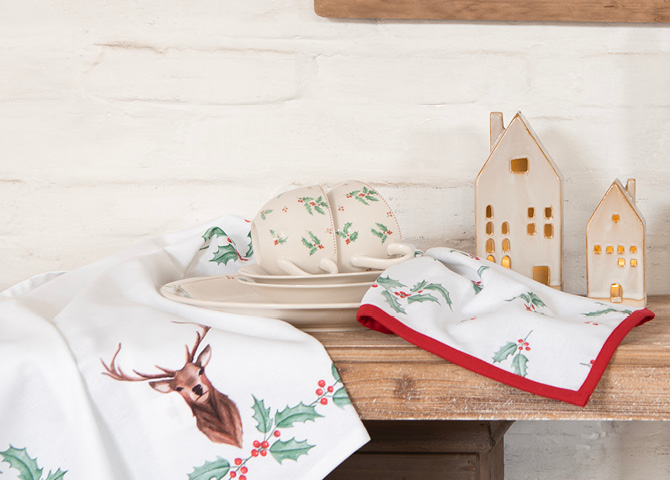 Weihnachtstextilien mit Geschirr, das Mistelzweige und dekorative Häuschen zeigt