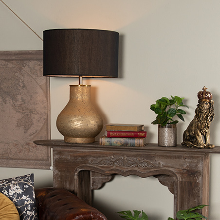 Cheminée brune avec une lampe de table dorée et un abat-jour noir, des livres et une statue de lion