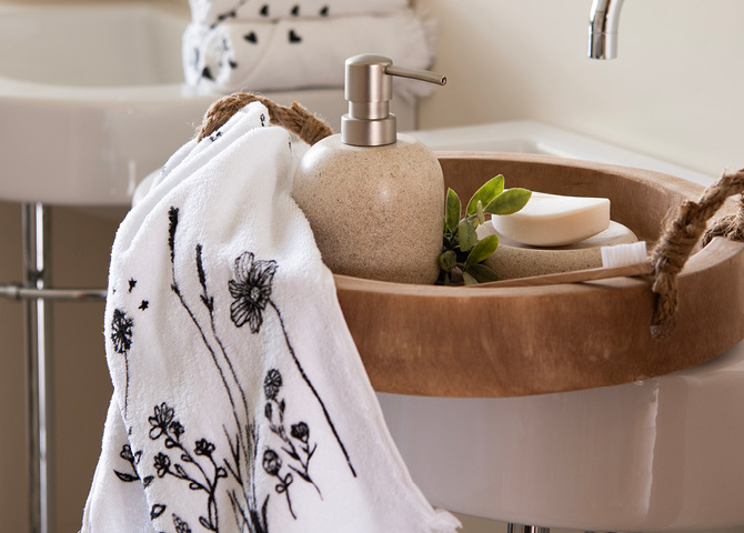 A wooden round tray with a soap holder, guest towel, toothbrush, and soap dish with soap