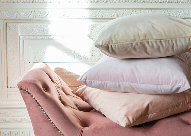 A blush pink bench with stacked solid pillows in colors like beige, light pink, and peach