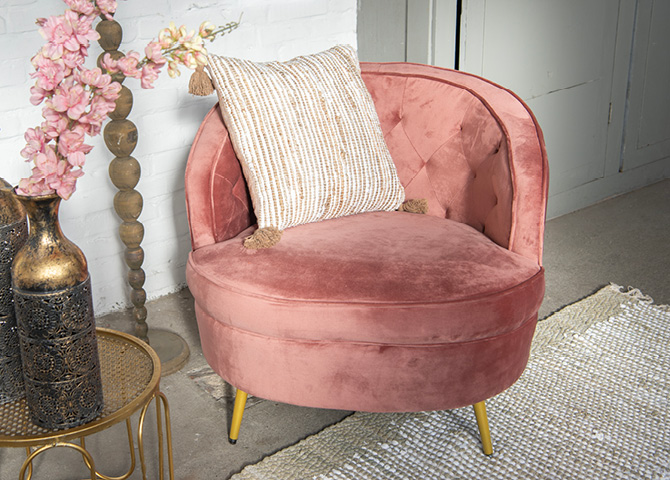 Een grote roze fauteuil met een geel en witte sierkussen in een gezellig zithoekje