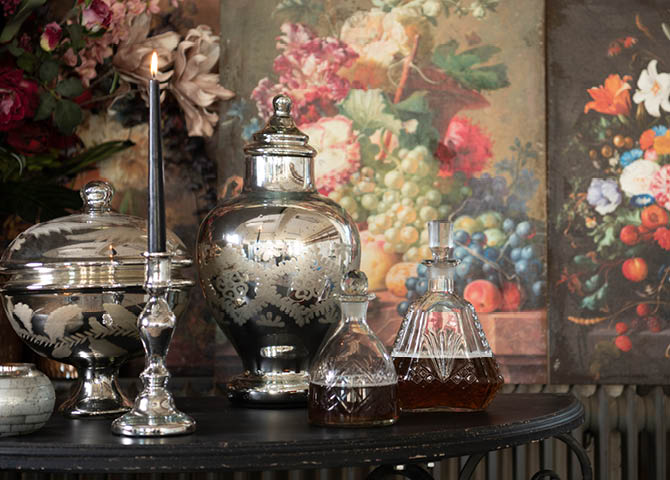 A table with vases, pitchers, and a candlestick, with wall decor in the background.