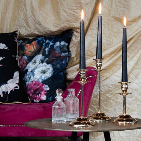 A side table with candlesticks and glass pitchers, with a sofa and cushions in the background.
