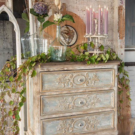 Une armoire avec des plantes, des vases de fleurs et des bougeoirs avec des bougies allumées.
