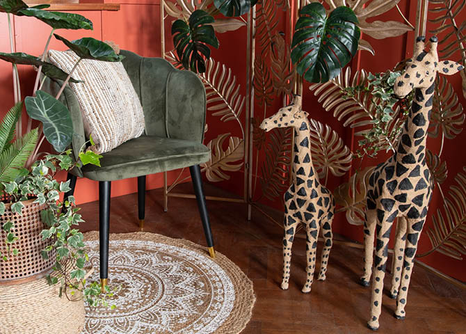 Un tapis, une chaise avec un coussin, des plantes et des statues de girafes.