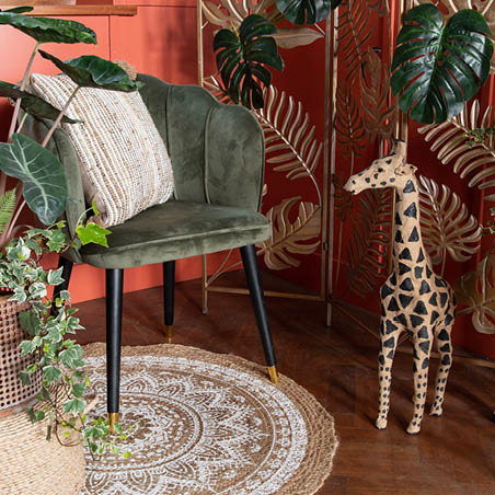 Un tapis, une chaise avec un coussin, des plantes et une statue d'une girafe.