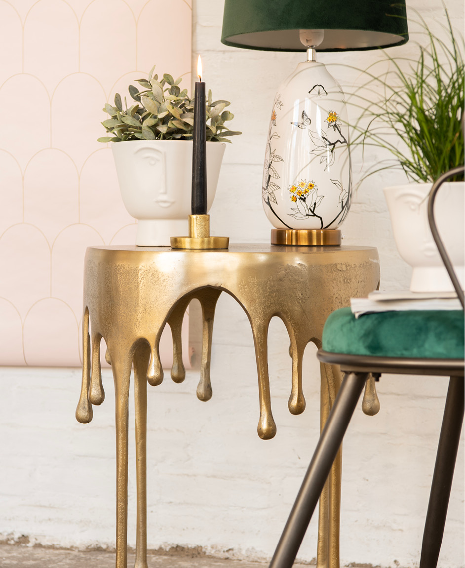Une table d'appoint, un bougeoir avec une bougie allumée, des pots de fleurs, une lampe de table et une chaise.