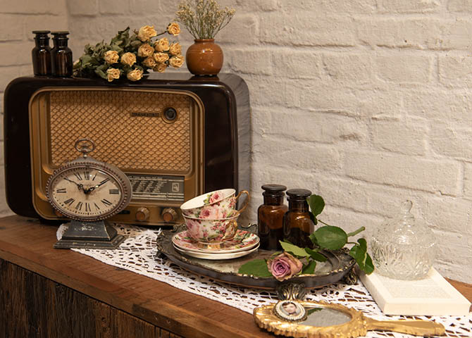 An old radio, a clock, a tray with teacups and saucers, a mirror, and a jewelry box.