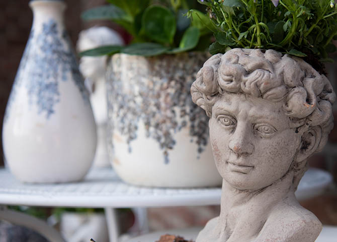 In the foreground, a figurine, and in the background, flowerpots on a table.