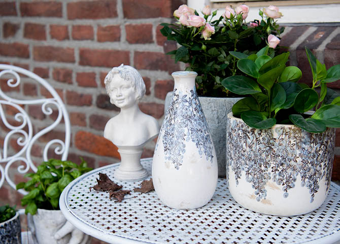 Een tafeltje met bloempotten, een beeldje en een vaas.