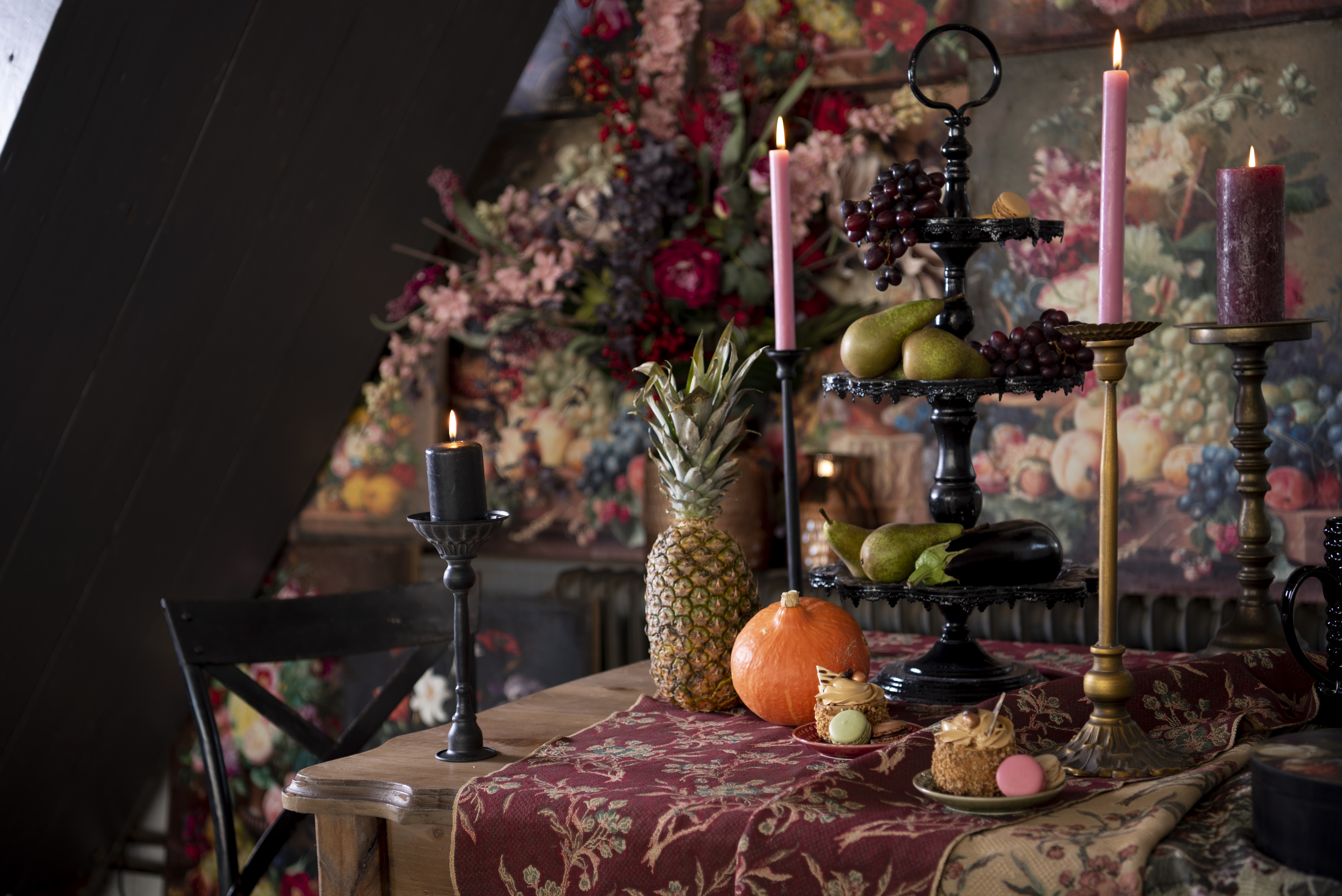 A table with a tablecloth, candleholders, plates, and an étagère. In the background, you can see wall decoration.
