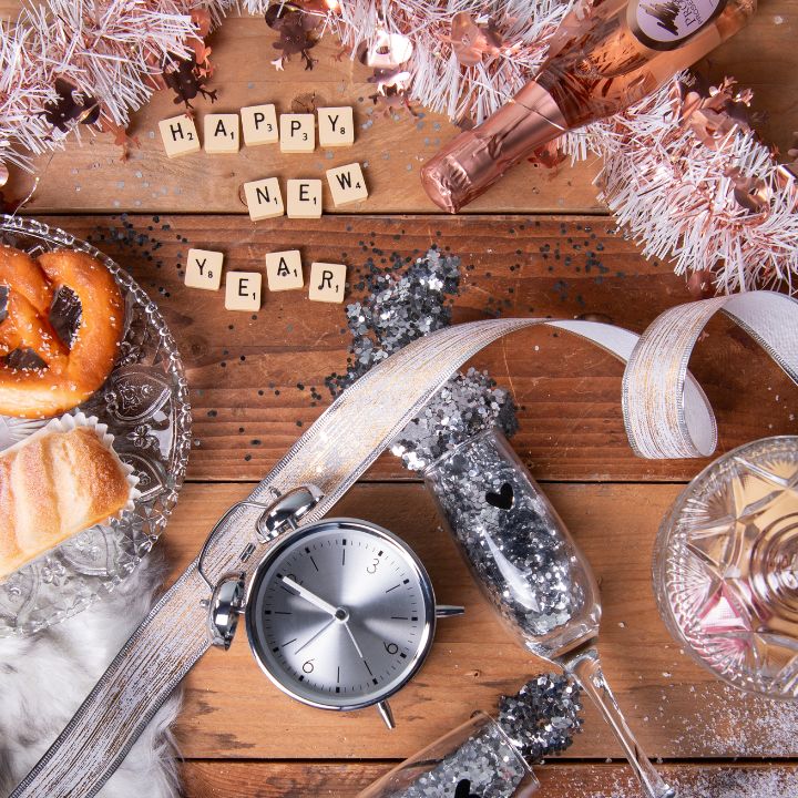 Three champagne flutes filled with champagne, next to a champagne bottle, surrounded by festive New Year's decorations such as streamers.  At the bottom of the image is a button labeled 'New Year,' linking to the New Year page.