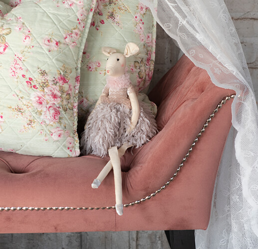 Een kleine muizenpop zit op een roze stoel met groene kussens met een roze bloemenpatroon op de achtergrond.