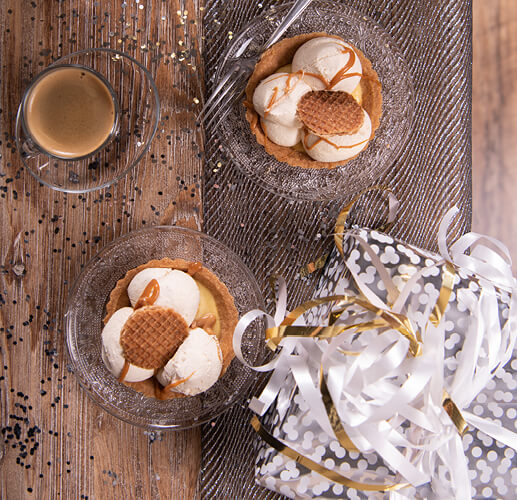 Two desserts with ice cream and stroopwafel are displayed in glass bowls, with a gift beside them. 