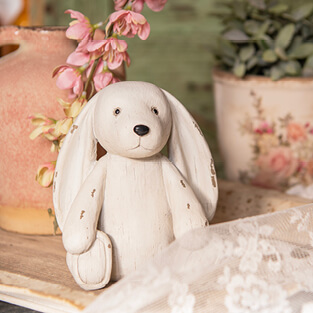 Niedliches weißes Stoffkaninchen inmitten romantischer Blumentöpfe, mit einem Knopf am unteren Rand des Fotos mit der Aufschrift 'Für Kinder', der auf Geschenke für Kinder hinweist.