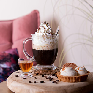 Een afbeelding van een kop koffie met een toef slagroom, een gebakje, en een glas met een borrel, keurig naast elkaar gepresenteerd. Aan de onderkant van de afbeelding bevindt zich een knop met het label 'Vaderdag', die linkt naar de Vaderdag pagina.