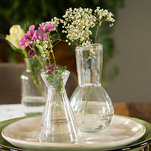 Twee kleine glazen vaasjes gevuld met bloemen.