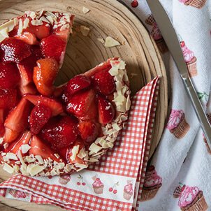 Eine Erdbeertorte auf einem Holzteller serviert, begleitet von einem rot-weiß karierten Serviette.