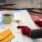 Landkarte auf einem Auto mit einer grünen Tasse, Schlüsselbund und jemandem, der mit roten Handschuhen zeigt