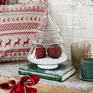 A glass cloche in the shape of a Christmas tree filled with fake snow and two red Christmas ornaments