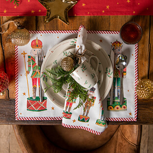 Een gedekte kersttafel met een placemat, dinerbord, ontbijtbord, kerstmok en een kerstservet