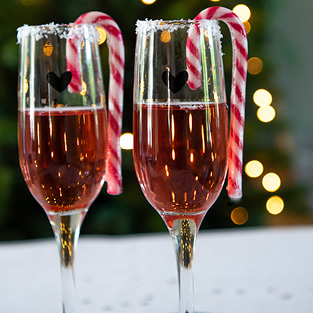 Two champagne glasses with a black heart on them and candy canes inside