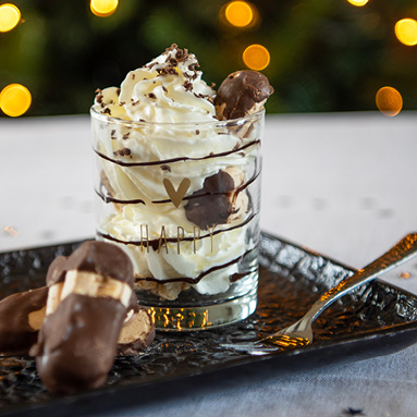 A drinking glass filled with whipped cream and cookies on a black metal tray