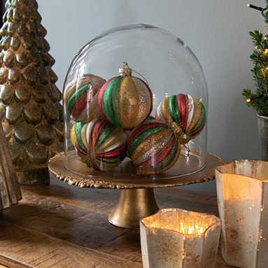 A gold-colored cake stand with a dome, containing colorful Christmas ornaments