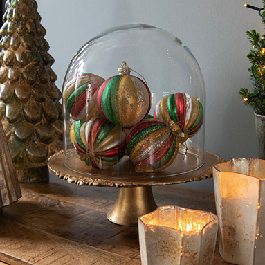 Een goudkleurige taartplateau met een stolp en daarin kleurrijke kerstballen