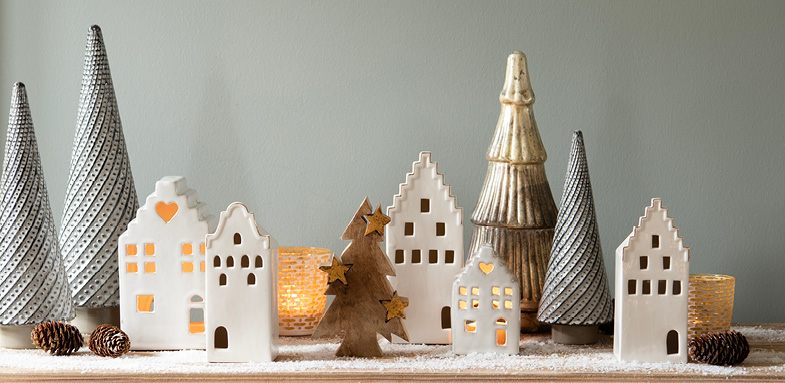 A scene of Christmas decorations, including a wooden Christmas tree, ceramic decorative houses, gray Christmas trees, gold Christmas trees, and yellow tealight holders