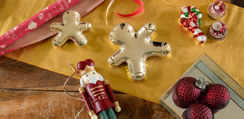 A wooden table filled with gold bowls, a red nutcracker, red Christmas ornaments, Christmas decorations, and red wrapping paper