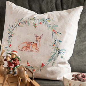 A white decorative pillow with a deer and a green wreath