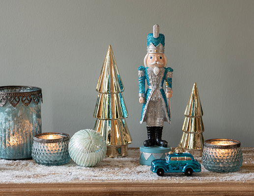 A blue nutcracker with two gold Christmas trees, a blue Christmas ornament, a light blue bauble, and three blue tealight holders