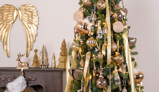 De gouden kersttrend met een kerstboom gevuld met goudkleurige ornamenten en kerstballen en een bruine schouw met een goudkleurige kerstsokhanger en drie goudkleurige kerstboomfiguren en gouden vleugels aan de muur