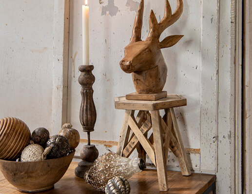 Een houten hertenkop op een houten krukje en een houten kandelaar met kerstballen in natuurlijke kleuren