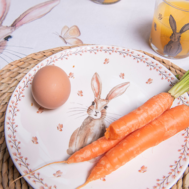 Een ontbijtbord met een konijn erop en op het bord ligt een ei en drie wortels