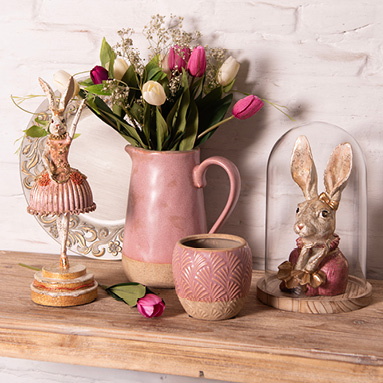 Easter decoration with a rabbit statue, pink flower pots and vases with tulips, and a glass cloche with an Easter bunny statue