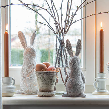 Rustieke paasdecoratie met fotolijsten, bloempotten, zilverkleurige konijnen beelden en decoratie ei