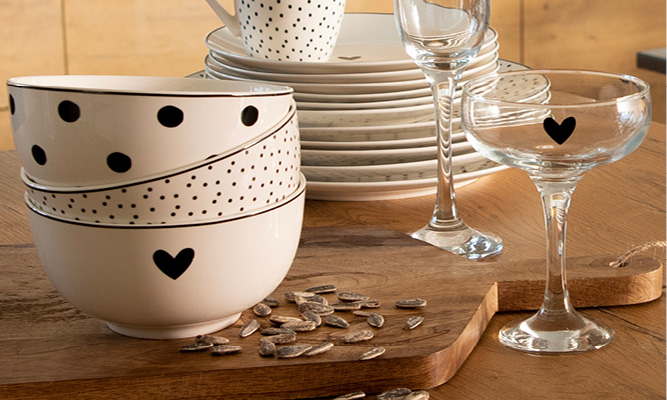 Three stacked modern bowls and a martini glass with a black heart on a wooden cutting board