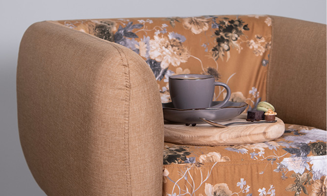 A vintage armchair with a wooden tray on which a modern cup and saucer with pastries are placed