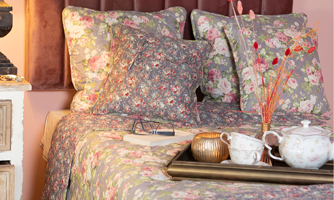 A made bed with romantic pillows and bedspread, and on the bed is a gold tray with tea cups and a teapot