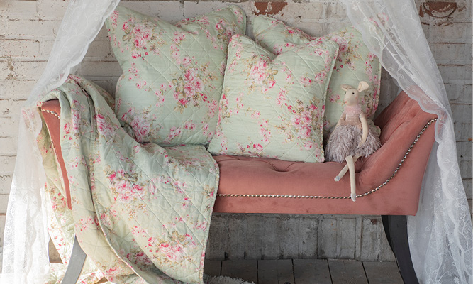 A dusty pink bench with three romantically green cushions and bedspread, and a decorative stuffed animal