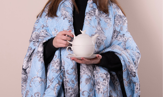 Someone with a folded blue bedspread holding a rural tea for one set