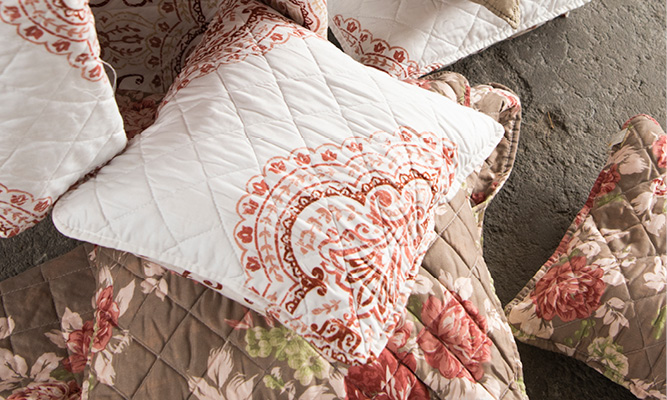 A stack of pillows with a white shabby chic pillow on top featuring Eastern patterns