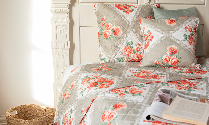 Ein ländlich gemachtes Bett mit romantischen Kissenbezügen und einer Bettdecke mit rosa Blumen und Pfingstrosen